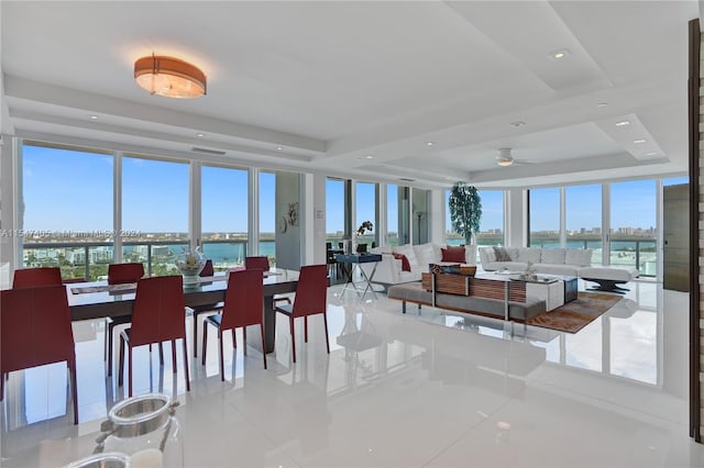 dining room featuring light tile patterned floors, ceiling fan, a water view, and a tray ceiling