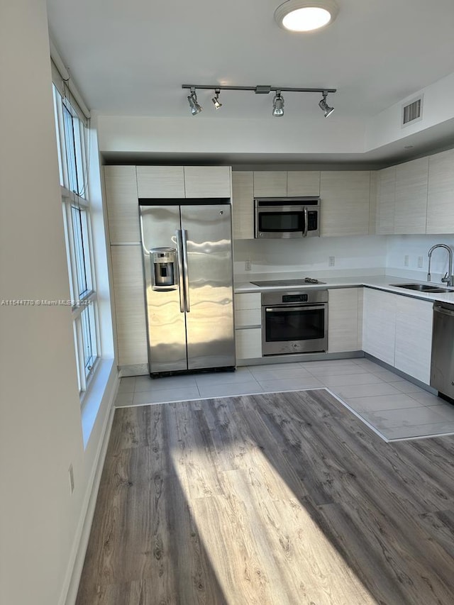 kitchen featuring appliances with stainless steel finishes, rail lighting, sink, and light hardwood / wood-style flooring