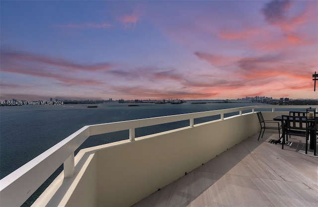 balcony at dusk featuring a water view