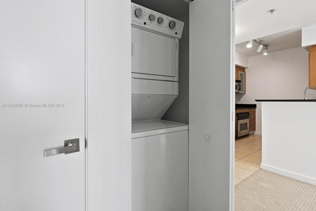 laundry area featuring light tile floors, stacked washing maching and dryer, and track lighting