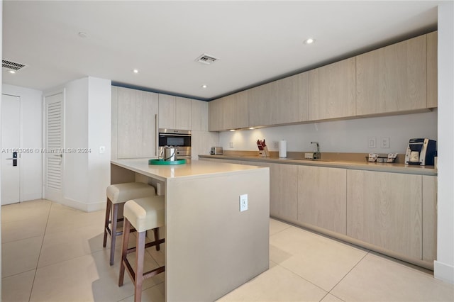 kitchen featuring light tile floors, light brown cabinets, stainless steel double oven, and a breakfast bar area