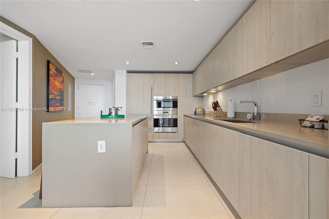 kitchen with light tile floors, double oven, a kitchen island, and sink