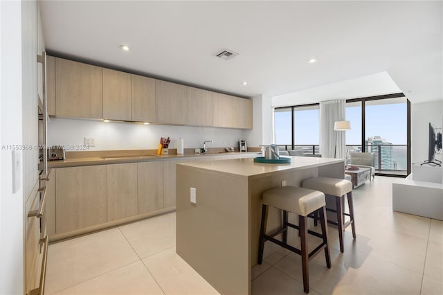 kitchen featuring light brown cabinetry, sink, a kitchen island, a breakfast bar, and light tile flooring