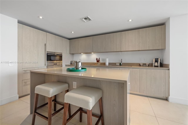 kitchen with light tile floors, a kitchen breakfast bar, a kitchen island, and light brown cabinetry