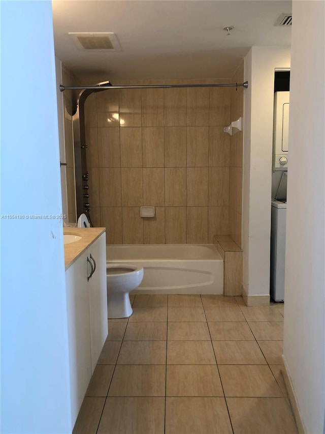 full bathroom with tiled shower / bath combo, vanity, stacked washer and clothes dryer, toilet, and tile patterned floors