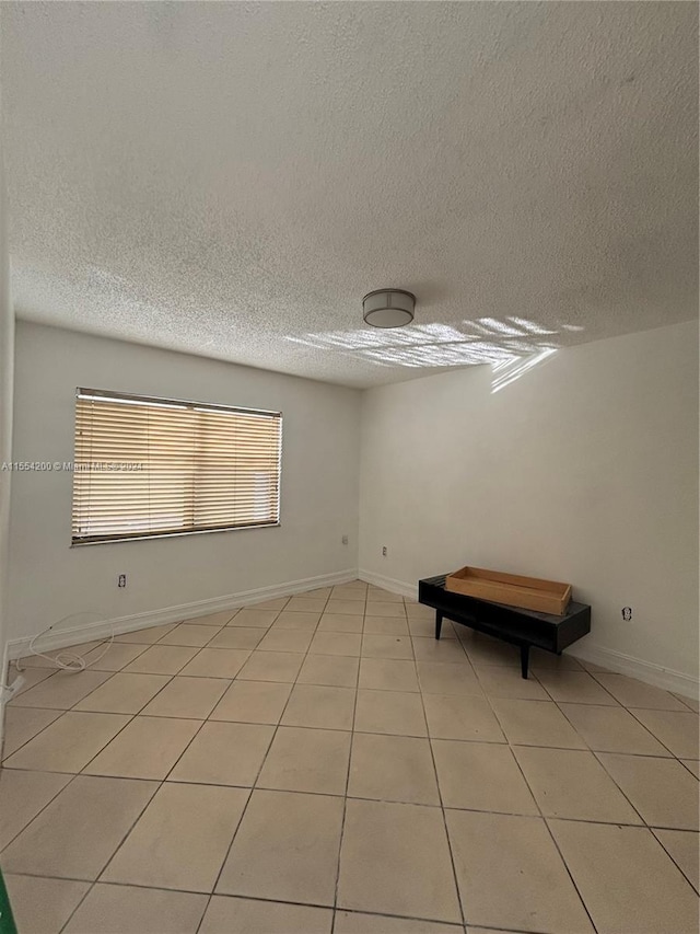 unfurnished room with light tile patterned floors, baseboards, and a textured ceiling