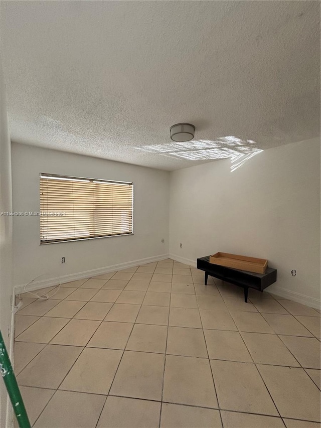 spare room featuring light tile patterned flooring, a textured ceiling, and baseboards