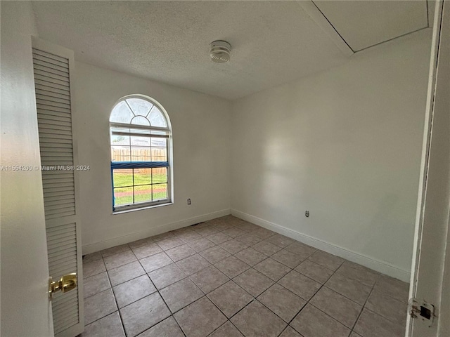 empty room featuring light tile patterned floors, baseboards, and a textured ceiling