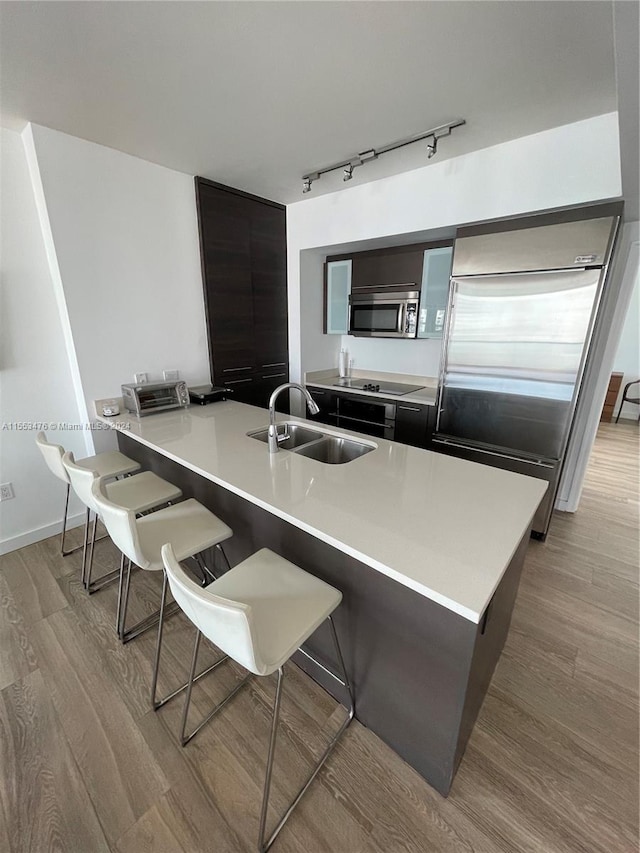 kitchen featuring sink, a kitchen breakfast bar, stainless steel appliances, track lighting, and light wood-type flooring