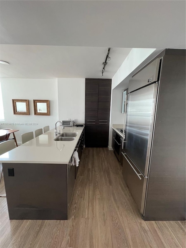 kitchen featuring sink, light hardwood / wood-style flooring, track lighting, stainless steel built in refrigerator, and dark brown cabinetry