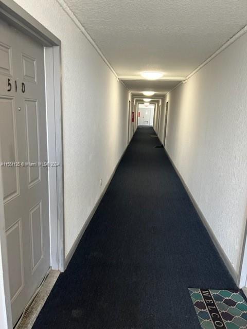 corridor featuring a textured ceiling and dark carpet