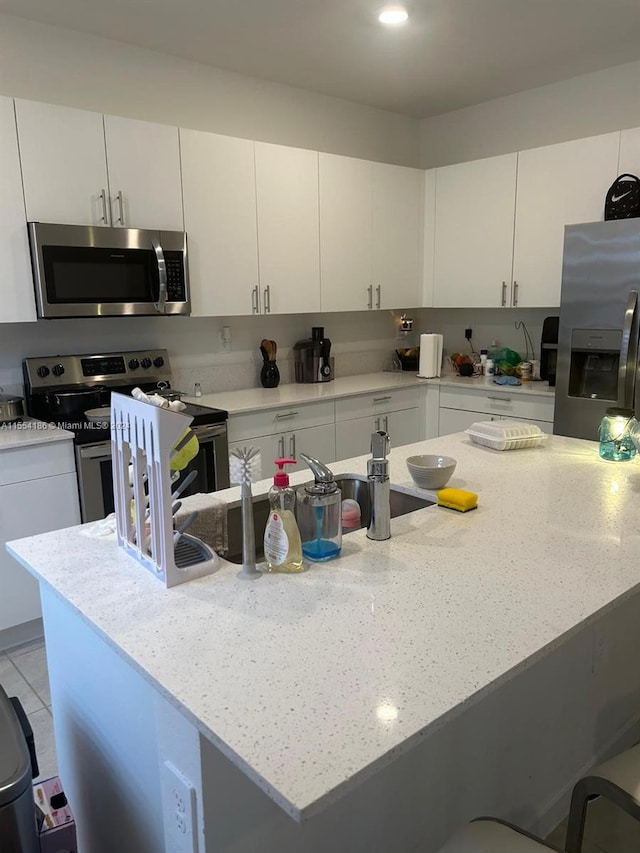 kitchen with white cabinetry, appliances with stainless steel finishes, sink, light stone counters, and a breakfast bar area