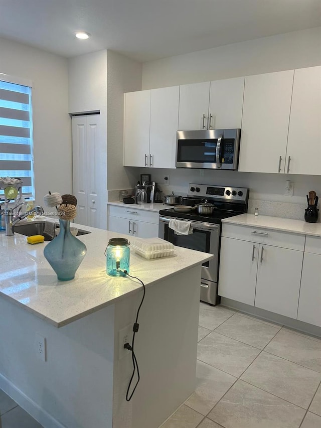 kitchen with sink, light tile floors, white cabinets, appliances with stainless steel finishes, and light stone countertops