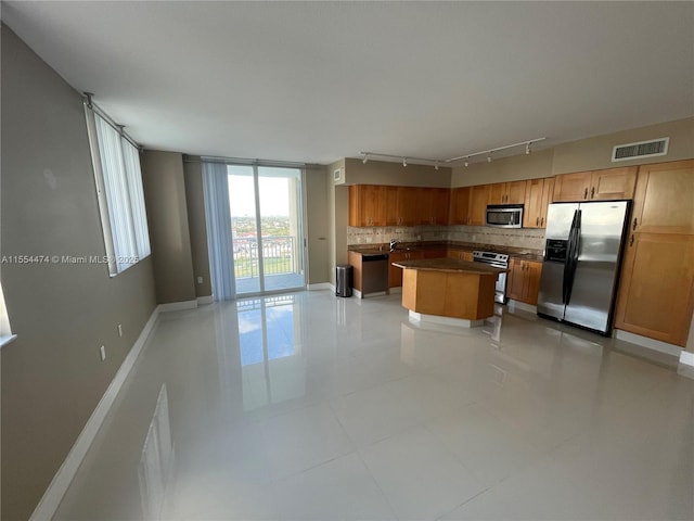 kitchen with light tile patterned flooring, track lighting, decorative backsplash, appliances with stainless steel finishes, and a kitchen island