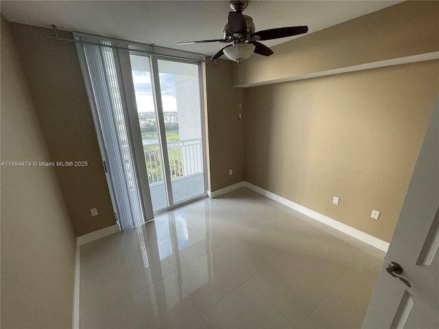 tiled empty room featuring ceiling fan and a wall of windows