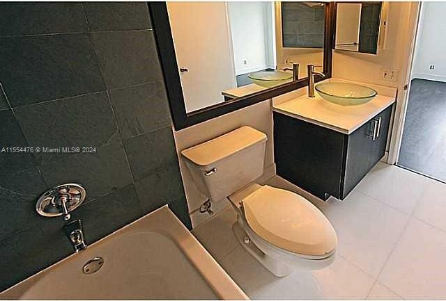 bathroom featuring toilet, vanity, a bath to relax in, and tile flooring