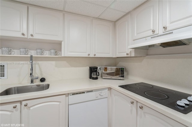 kitchen featuring white dishwasher, sink, a drop ceiling, and white cabinetry