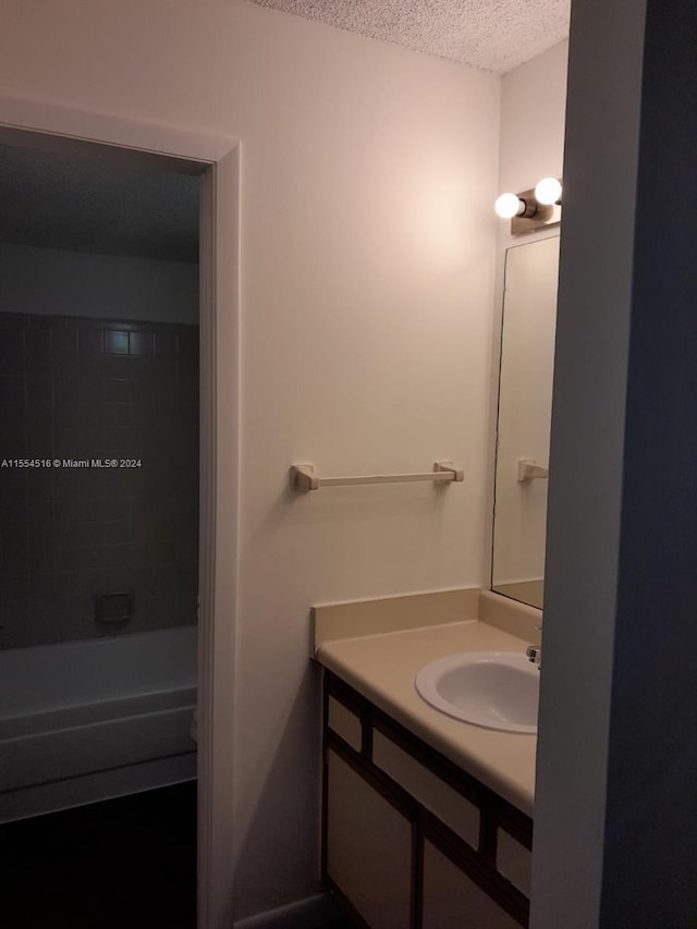 bathroom featuring a textured ceiling, tiled shower / bath combo, and vanity