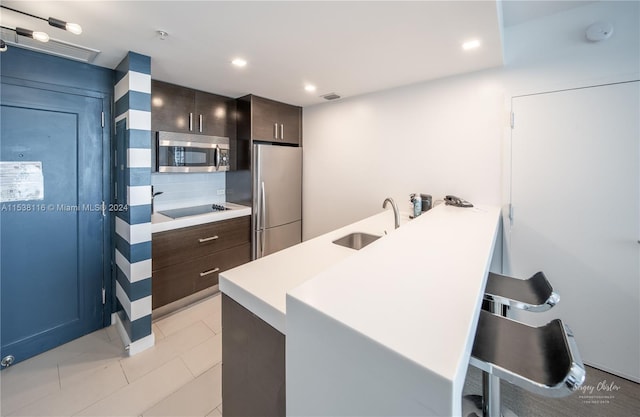 kitchen featuring appliances with stainless steel finishes, a kitchen bar, sink, kitchen peninsula, and light tile patterned flooring