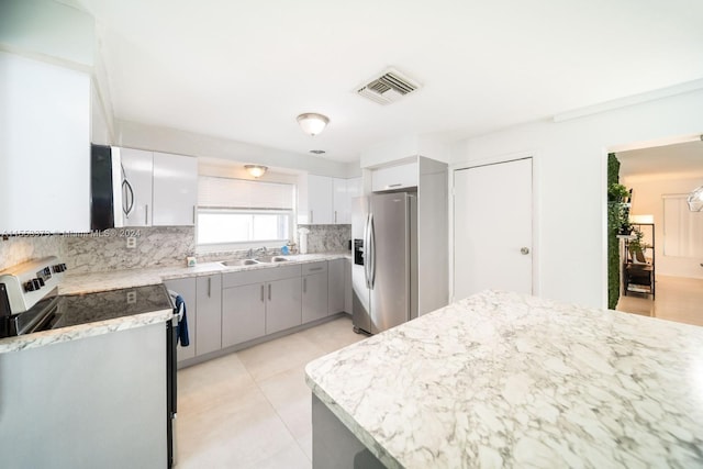 kitchen with light tile patterned floors, sink, gray cabinetry, appliances with stainless steel finishes, and decorative backsplash