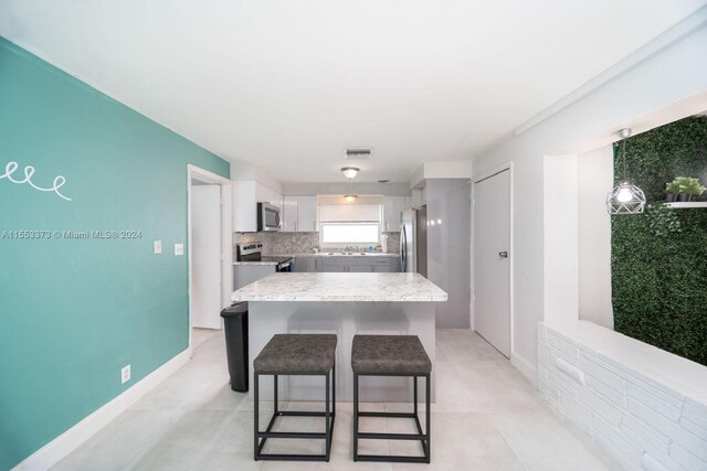 kitchen featuring white cabinets, appliances with stainless steel finishes, a center island, a breakfast bar area, and decorative backsplash