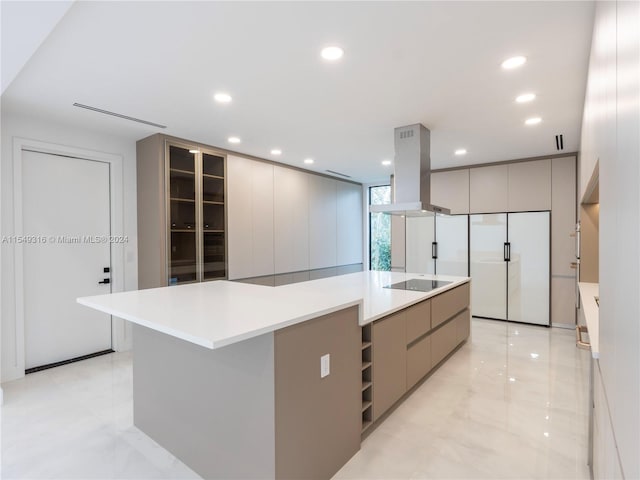 kitchen featuring gray cabinetry, black electric cooktop, an island with sink, light tile floors, and island range hood