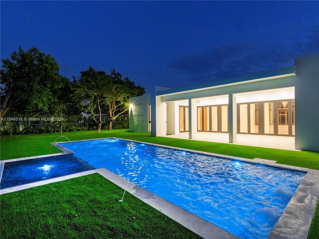 pool at twilight featuring pool water feature and a lawn