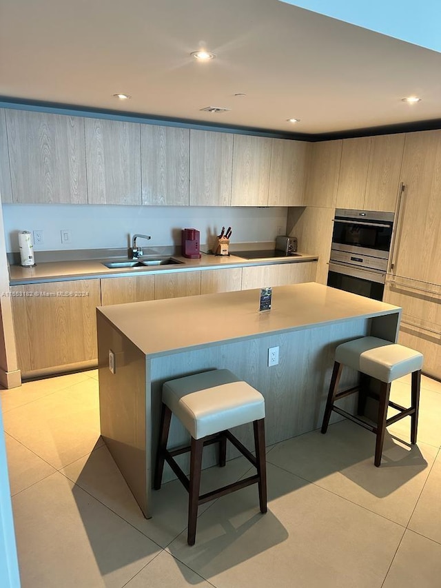 kitchen featuring a breakfast bar, a kitchen island, light brown cabinets, and sink