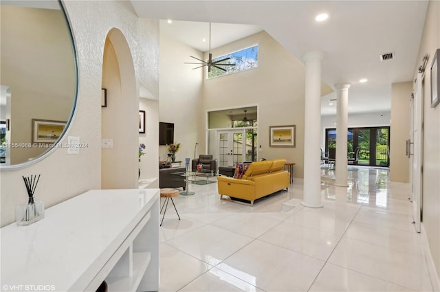 tiled living room featuring a high ceiling, decorative columns, and ceiling fan