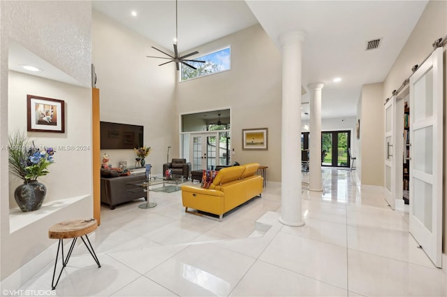 tiled living room with a towering ceiling, a healthy amount of sunlight, ceiling fan, and ornate columns