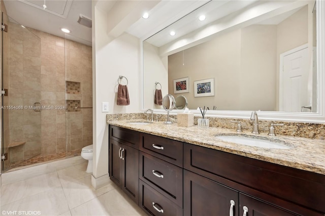 bathroom with a tile shower, tile floors, double vanity, and toilet