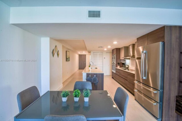 kitchen featuring light tile floors, appliances with stainless steel finishes, sink, and wall chimney range hood