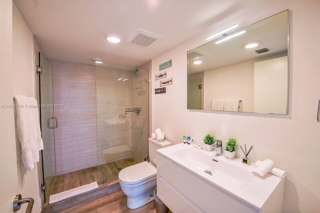 bathroom with an enclosed shower, toilet, large vanity, and hardwood / wood-style flooring