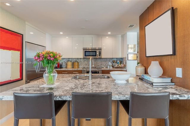 kitchen featuring appliances with stainless steel finishes, a kitchen bar, white cabinets, and light stone counters