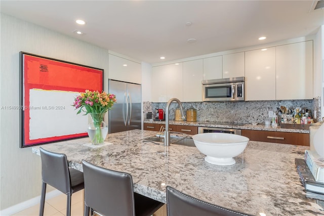 kitchen with white cabinetry, appliances with stainless steel finishes, a kitchen bar, light stone counters, and tasteful backsplash