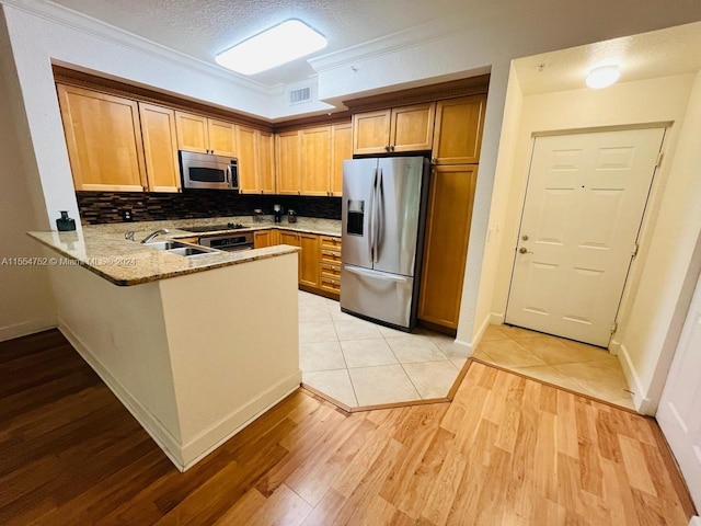 kitchen with kitchen peninsula, light tile floors, ornamental molding, appliances with stainless steel finishes, and stone counters