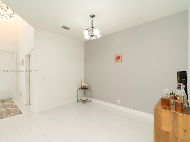 spare room featuring a chandelier, marble finish floor, visible vents, and baseboards