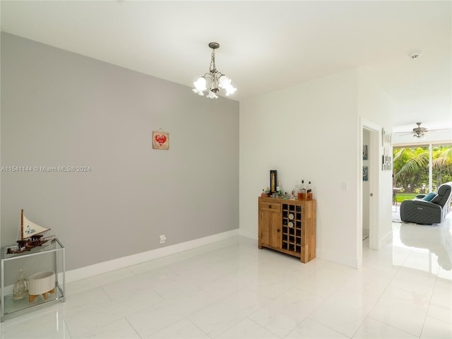 empty room with marble finish floor, baseboards, and ceiling fan with notable chandelier