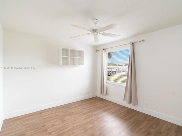 spare room featuring light wood finished floors, a ceiling fan, and baseboards