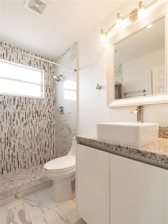 bathroom featuring toilet, marble finish floor, a tile shower, and visible vents