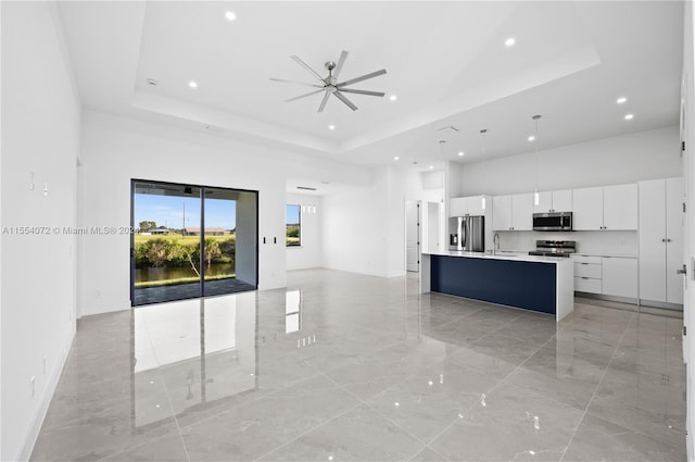 kitchen featuring stainless steel appliances, white cabinets, open floor plan, a center island with sink, and decorative light fixtures