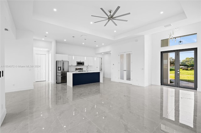 kitchen featuring open floor plan, a kitchen island with sink, stainless steel appliances, french doors, and white cabinetry