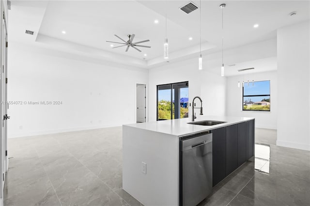 kitchen featuring a sink, light countertops, dishwasher, a raised ceiling, and a center island with sink