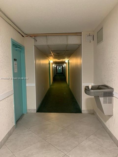 corridor with a textured ceiling and light tile floors