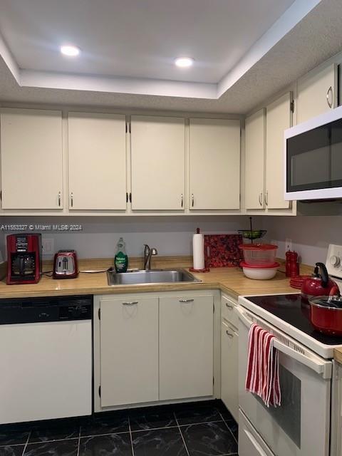 kitchen with white appliances, dark tile floors, sink, a tray ceiling, and white cabinetry