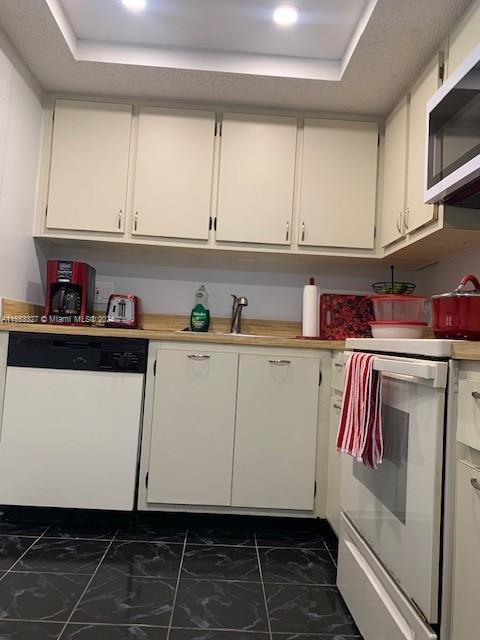 kitchen with white cabinets, white dishwasher, dark tile flooring, and range