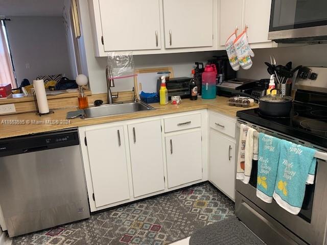 kitchen with dark tile flooring, white cabinetry, appliances with stainless steel finishes, and sink