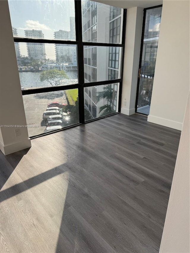 unfurnished room with a water view, dark wood-type flooring, and a wall of windows