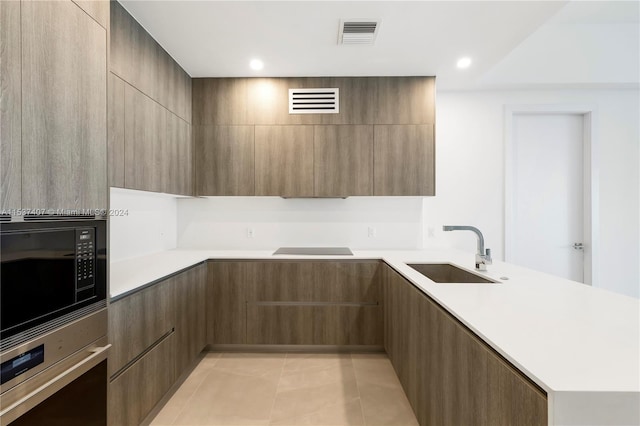 kitchen featuring black microwave, stainless steel oven, light tile patterned flooring, and sink