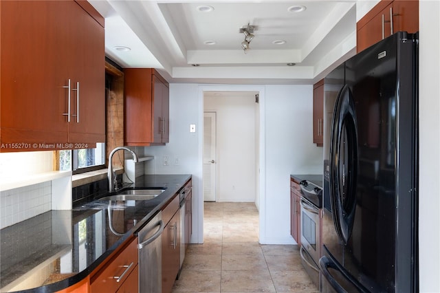 kitchen featuring sink, appliances with stainless steel finishes, dark stone counters, light tile patterned floors, and a tray ceiling